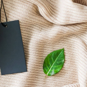 Ausschnitt eines hellbraunen Kleidungsstücks, darauf ein Preislabel und ein grüne Blatt – Symbolbild für nachhaltige Preisstrategie im E-Commerce.