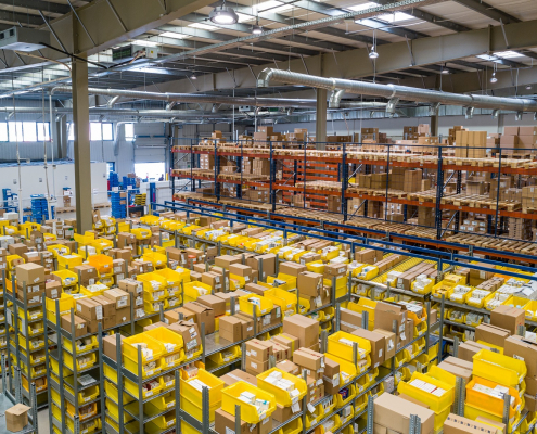 Das Bild zeigt einen großen Lagerraum mit einer Mege Kartons und gelben Boxen